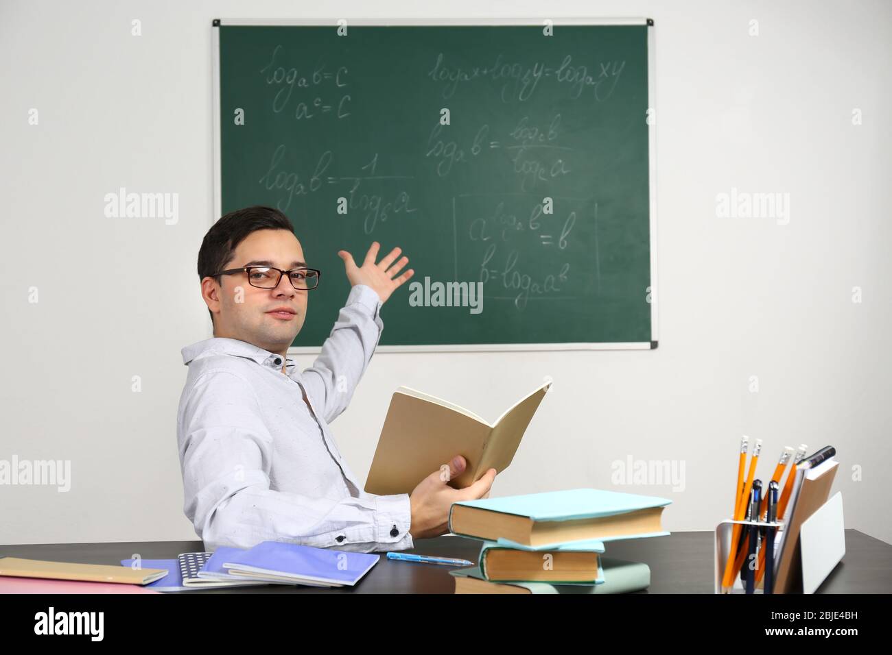 Handsome young teacher sitting at table in classroom Stock Photo