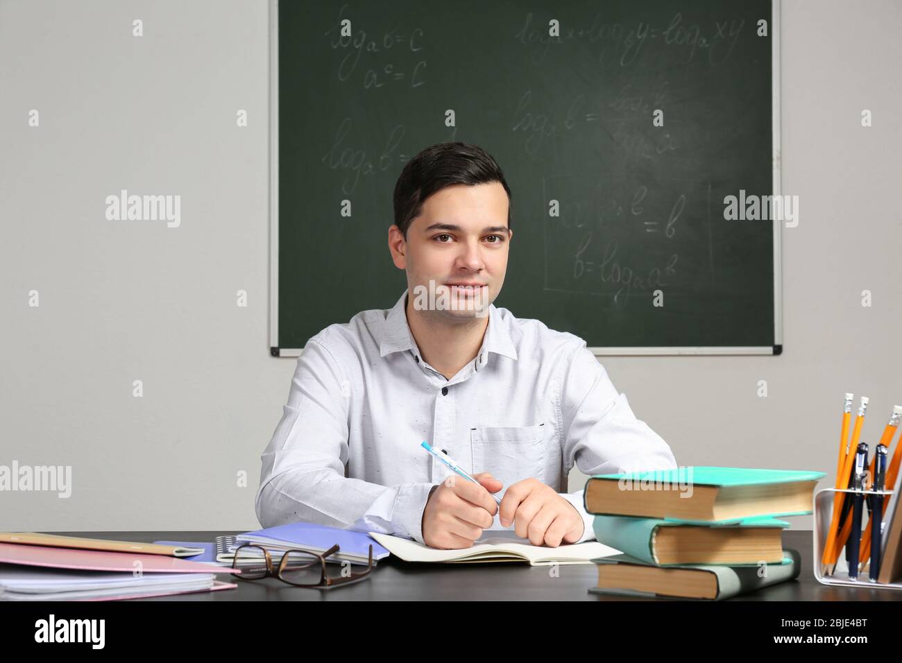 Handsome young teacher sitting at table in classroom Stock Photo