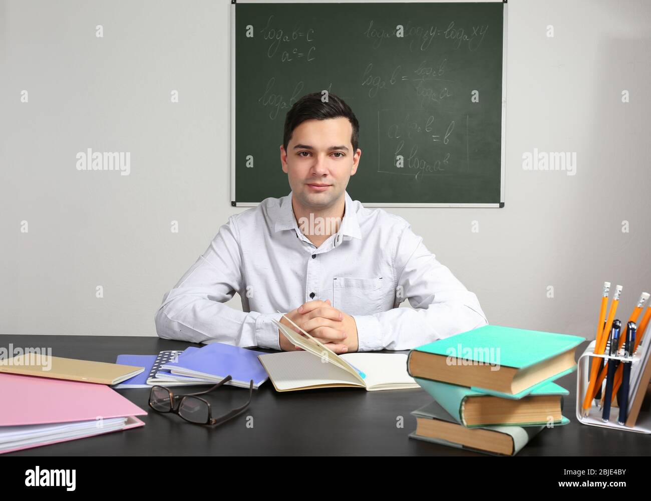 Handsome young teacher sitting at table in classroom Stock Photo