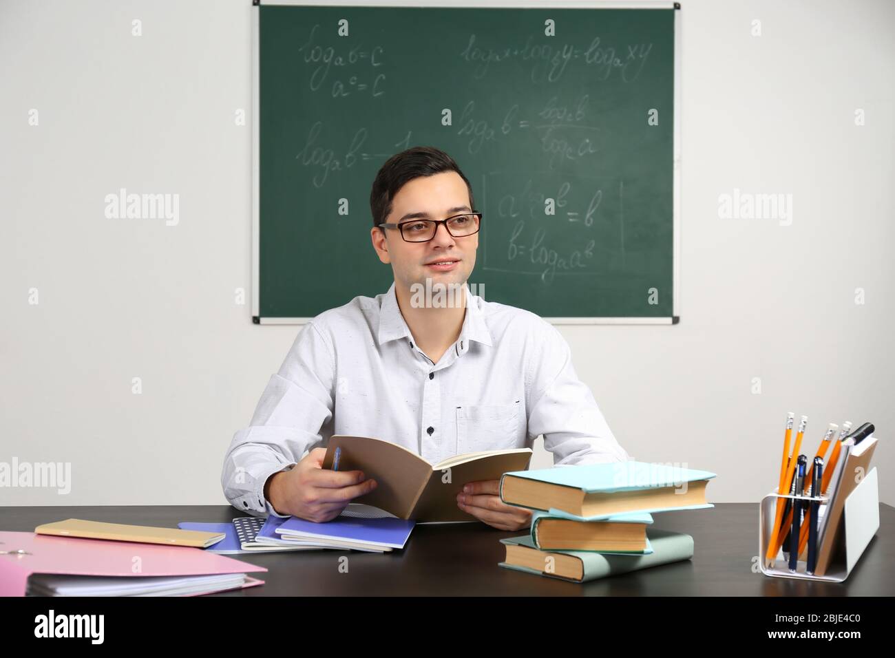 Handsome young teacher sitting at table in classroom Stock Photo