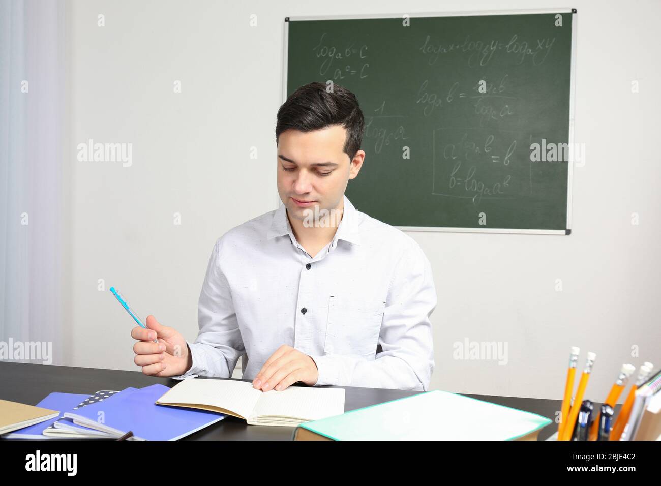 Handsome young teacher sitting at table in classroom Stock Photo