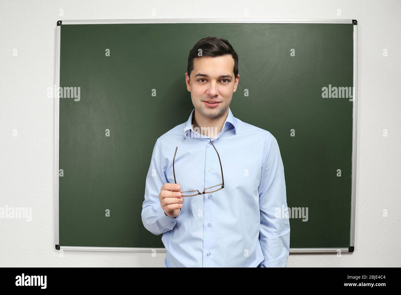 Handsome young teacher standing near blackboard in classroom Stock ...