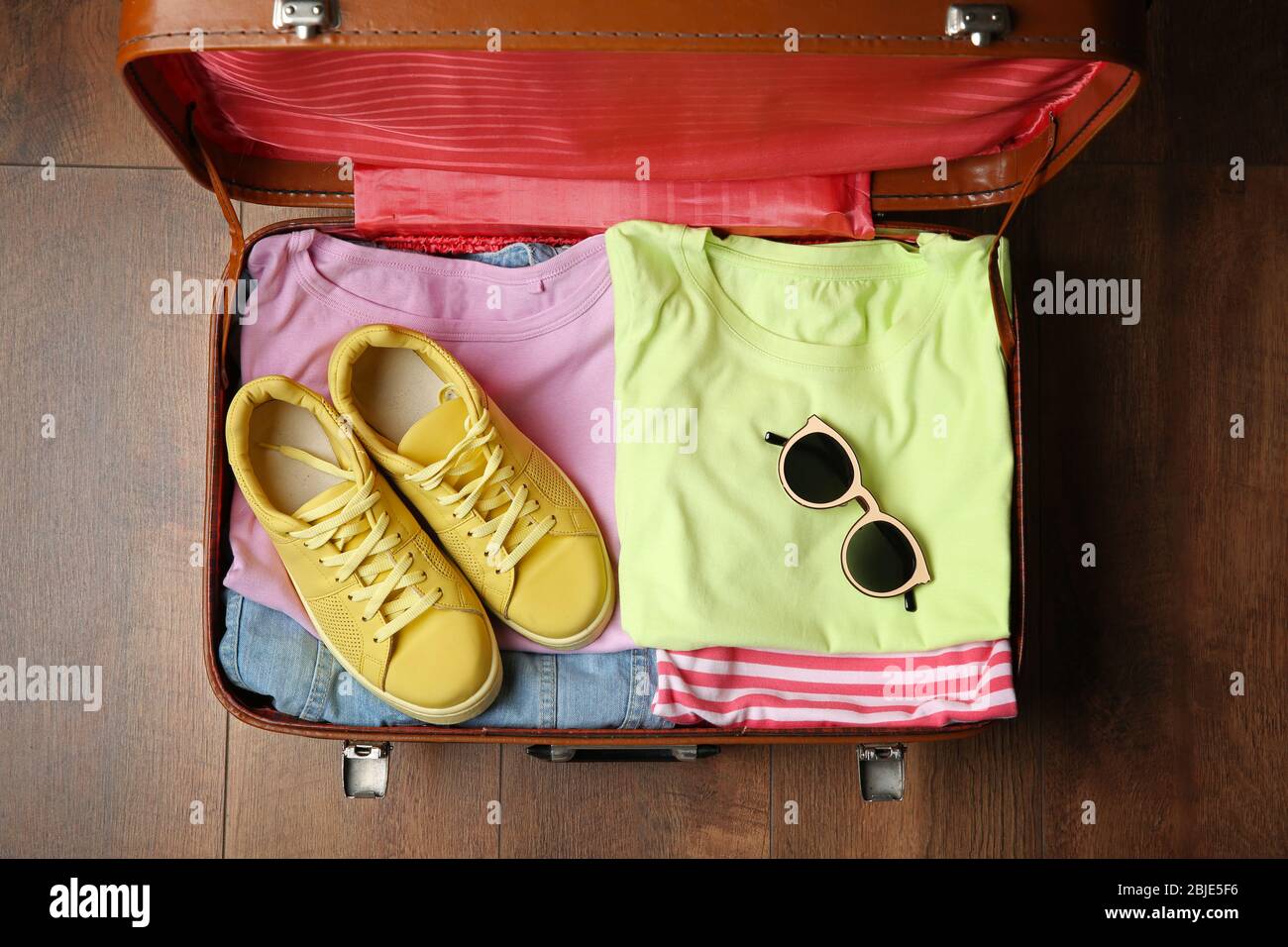 Open suitcase with clothes on wooden floor Stock Photo