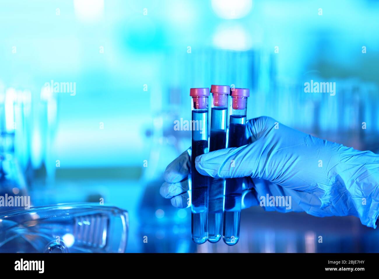 Hand in glove holding test tubes on blurred background Stock Photo - Alamy