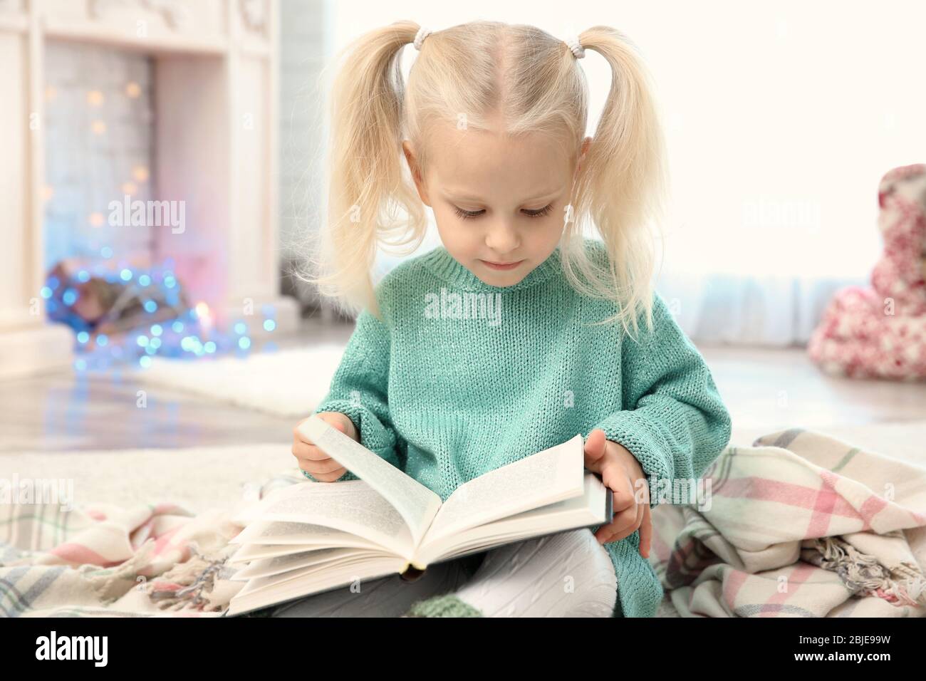 Cute little girl reading book at home Stock Photo - Alamy