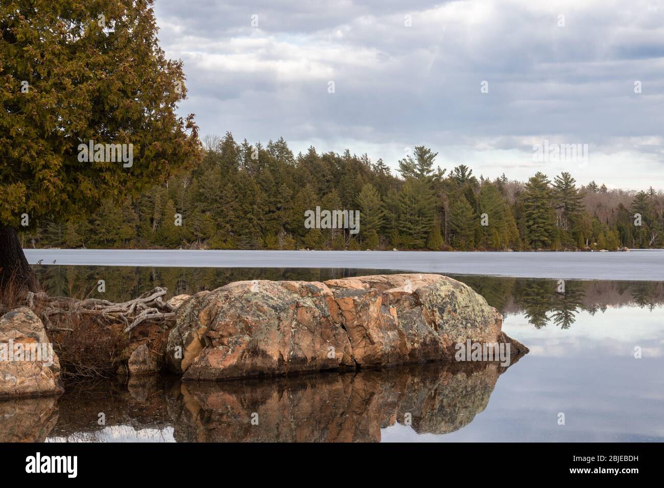 A large granite rock juts out from the shore on a beautiful lake in Algonquin Park in spring. Stock Photo