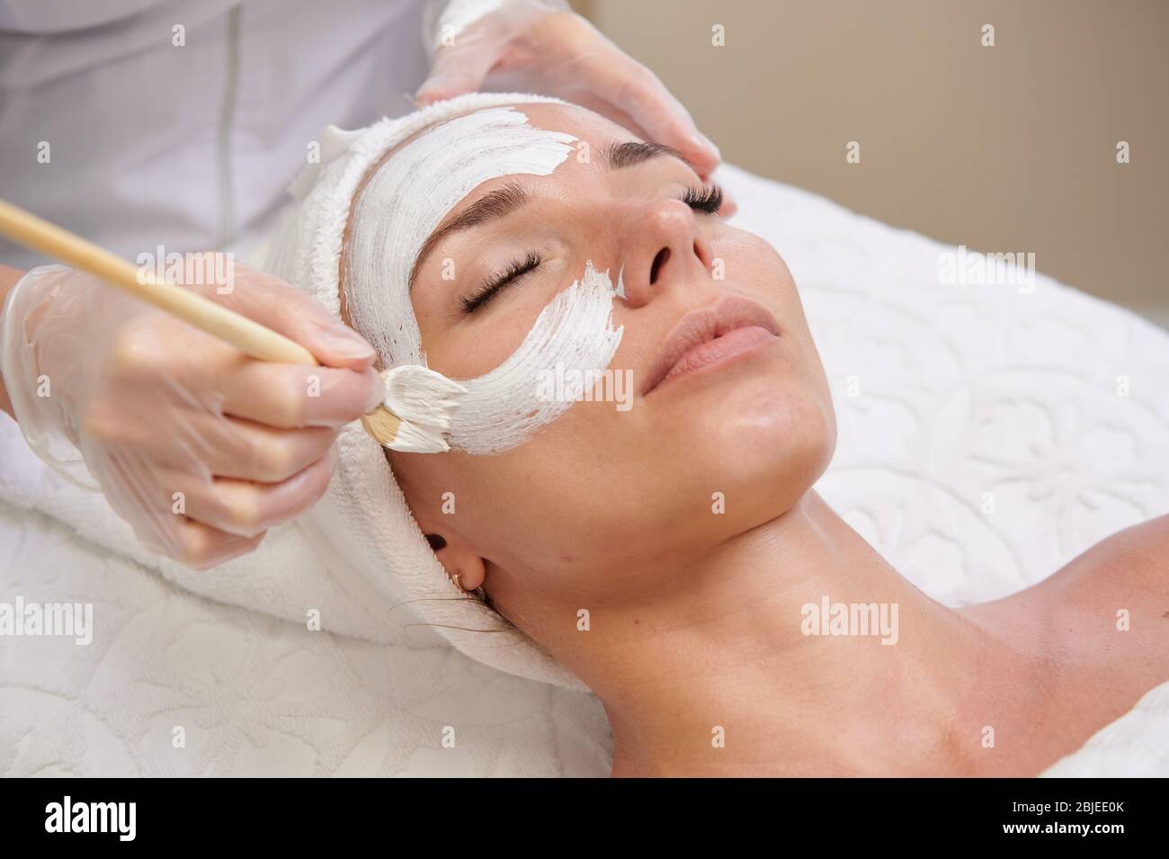 Applying white facial mask with brush in spa treatment alternative medicine Stock Photo