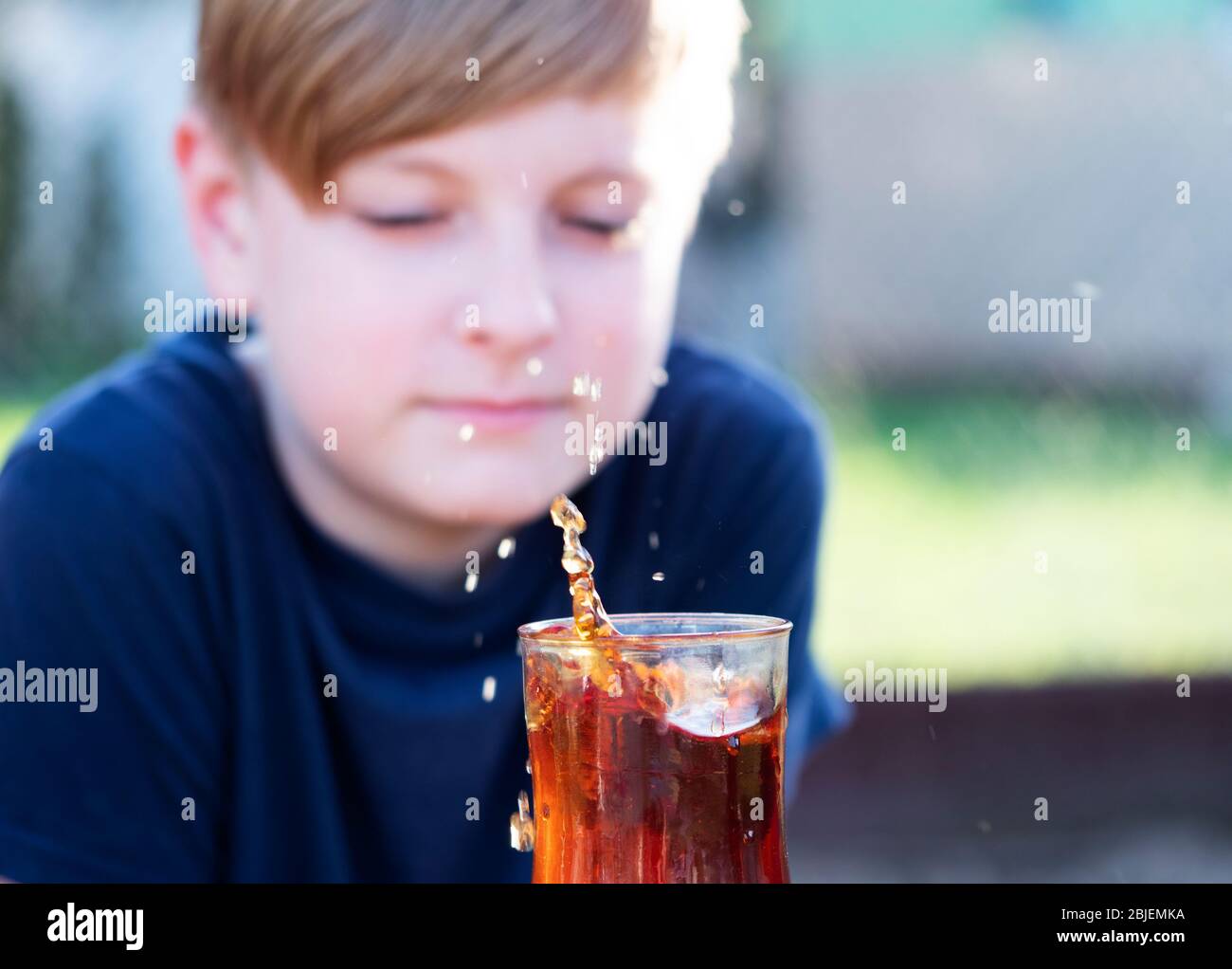 Caucasian boy watches a splash of tea in a cup from a falling piece of sugar Stock Photo
