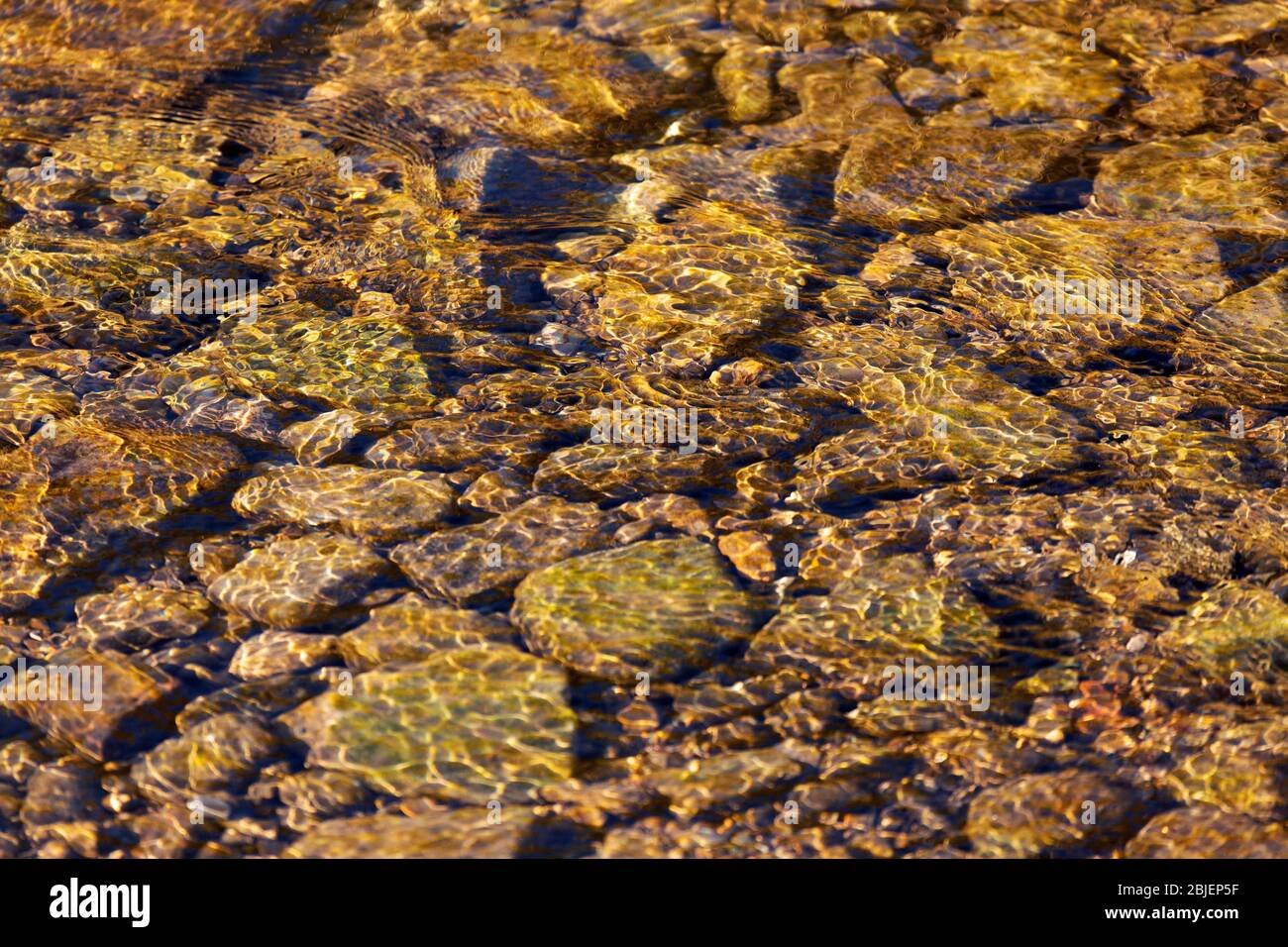 Rocks in a stream at Watergate Park in Gateshead, England. Sunshine refracts through the rippled surface of the waterway. Stock Photo