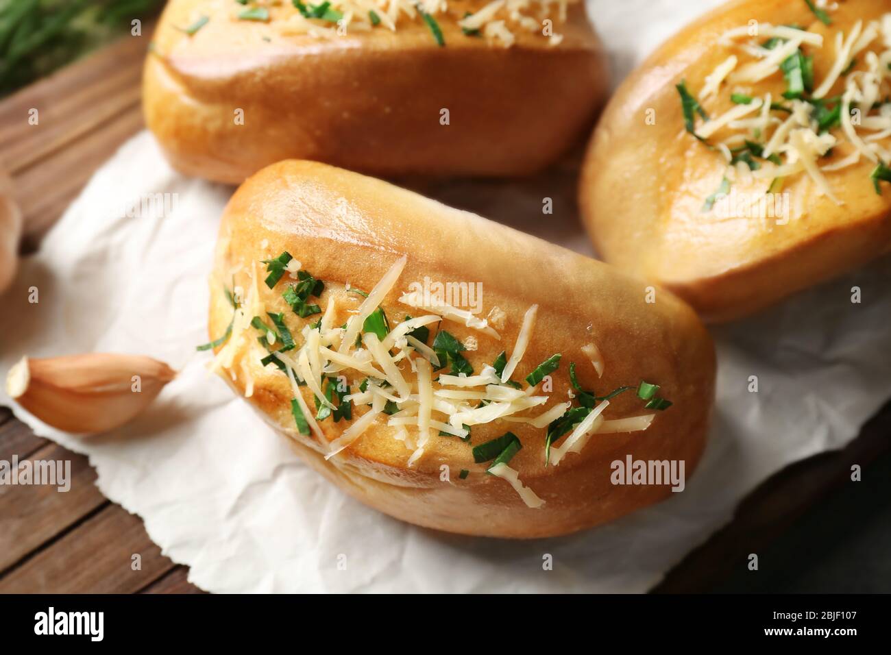 Tasty buns with garlic, cheese and herbs on paper Stock Photo