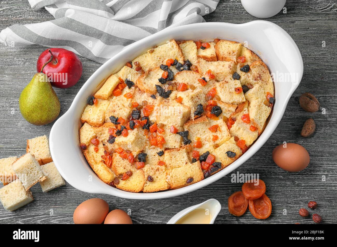 Freshly baked bread pudding in casserole dish and ingredients on wooden table Stock Photo
