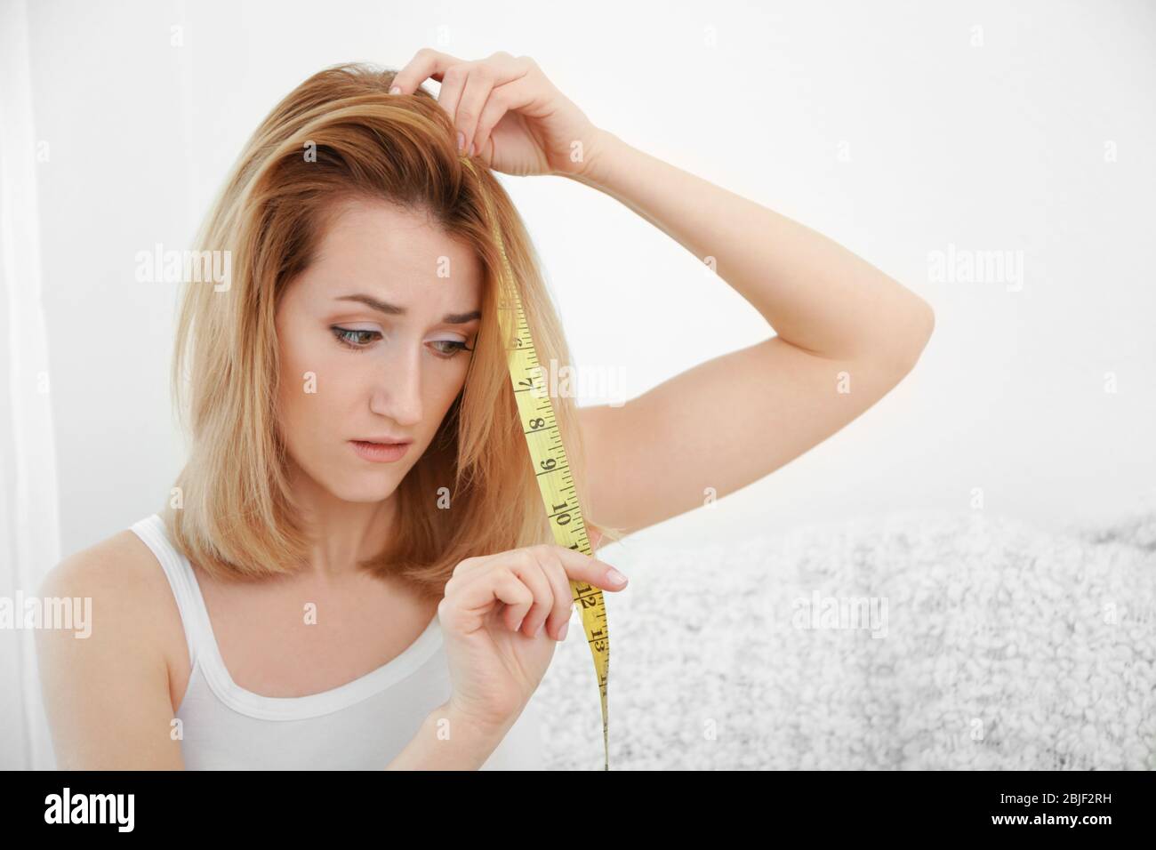 Beautiful young woman measuring length of hair at home Stock Photo