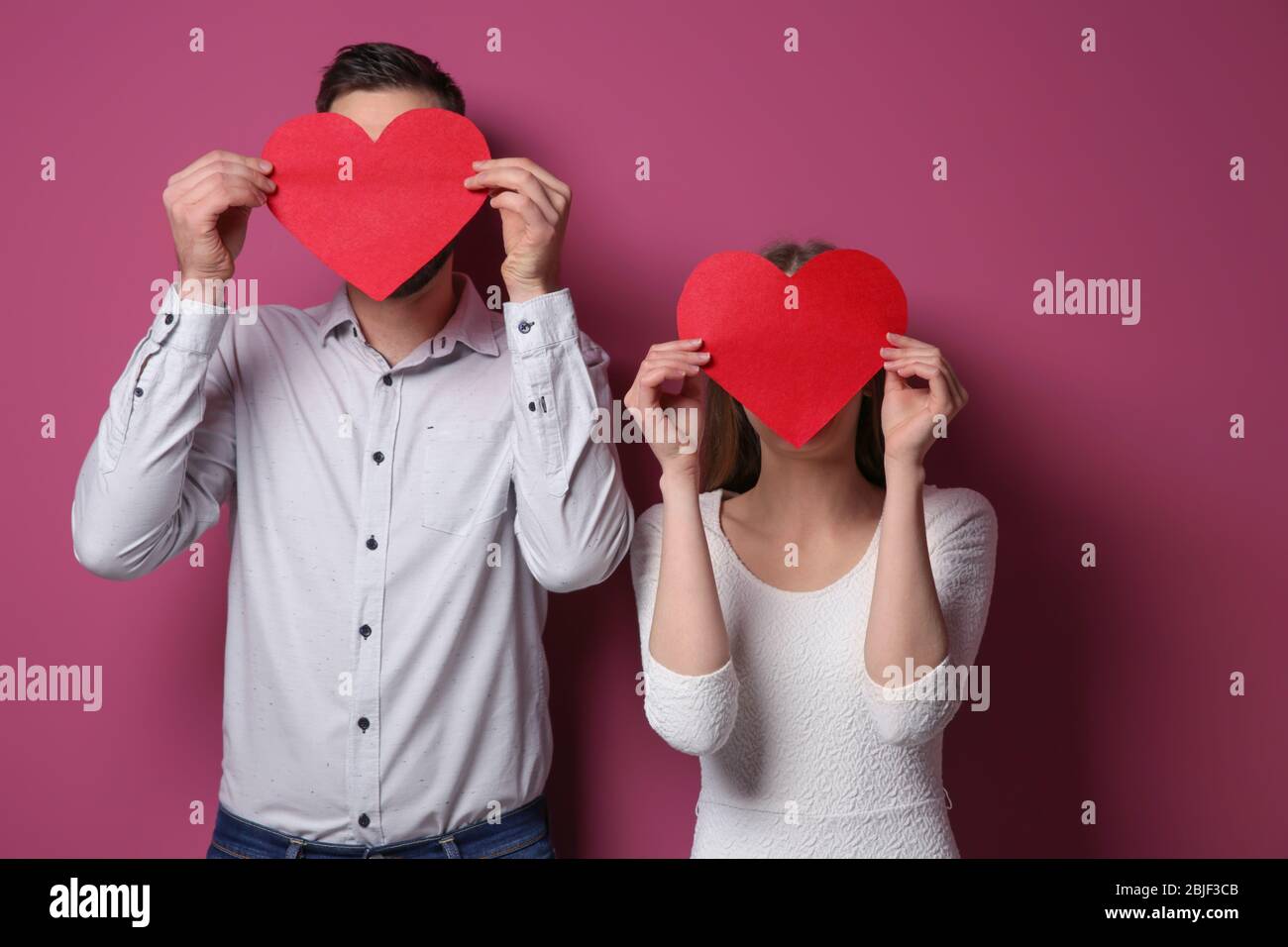 Happy young couple with red hearts on color background Stock Photo - Alamy