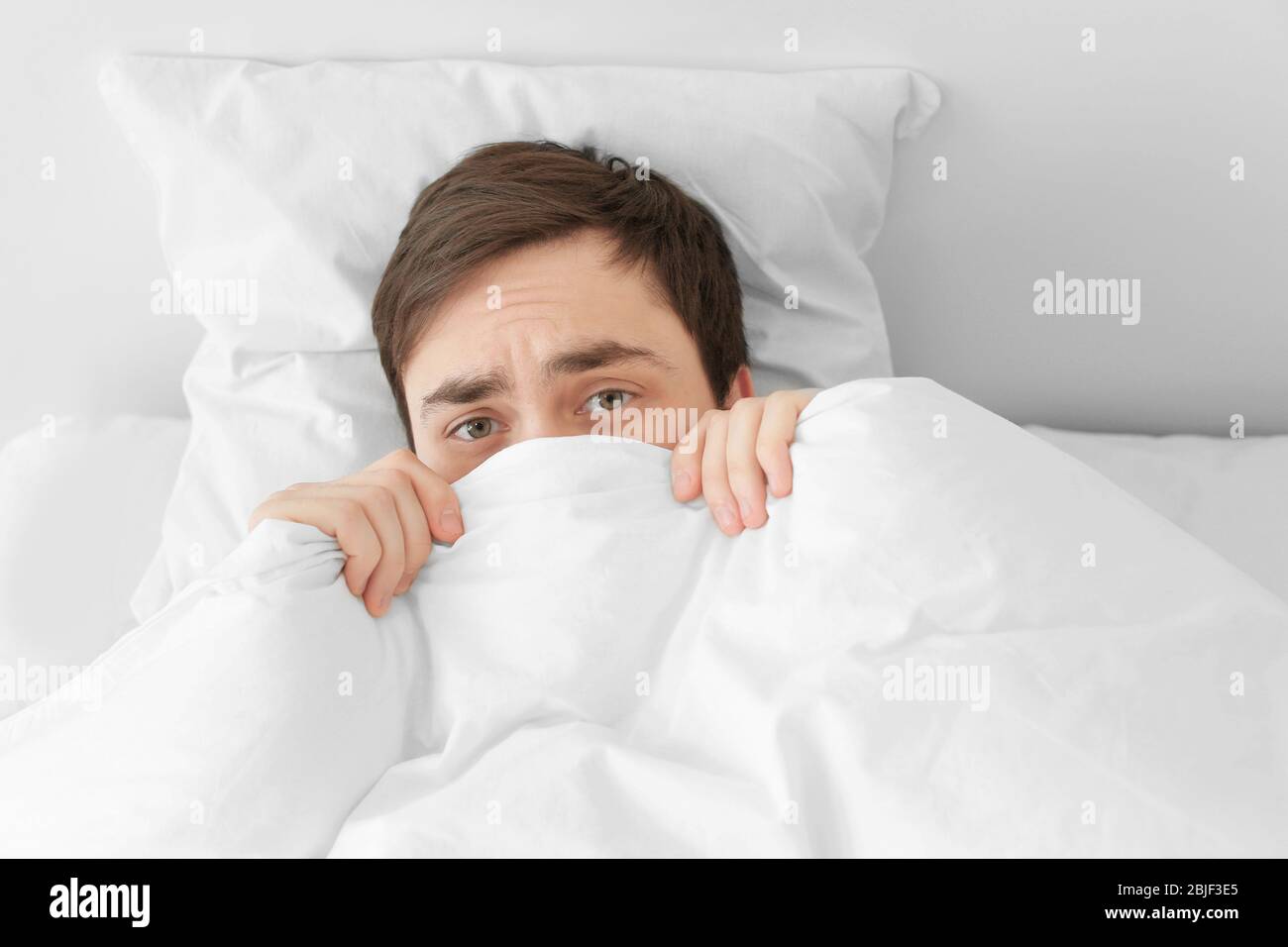 Young man hiding under blanket while lying in bed at home Stock Photo -  Alamy