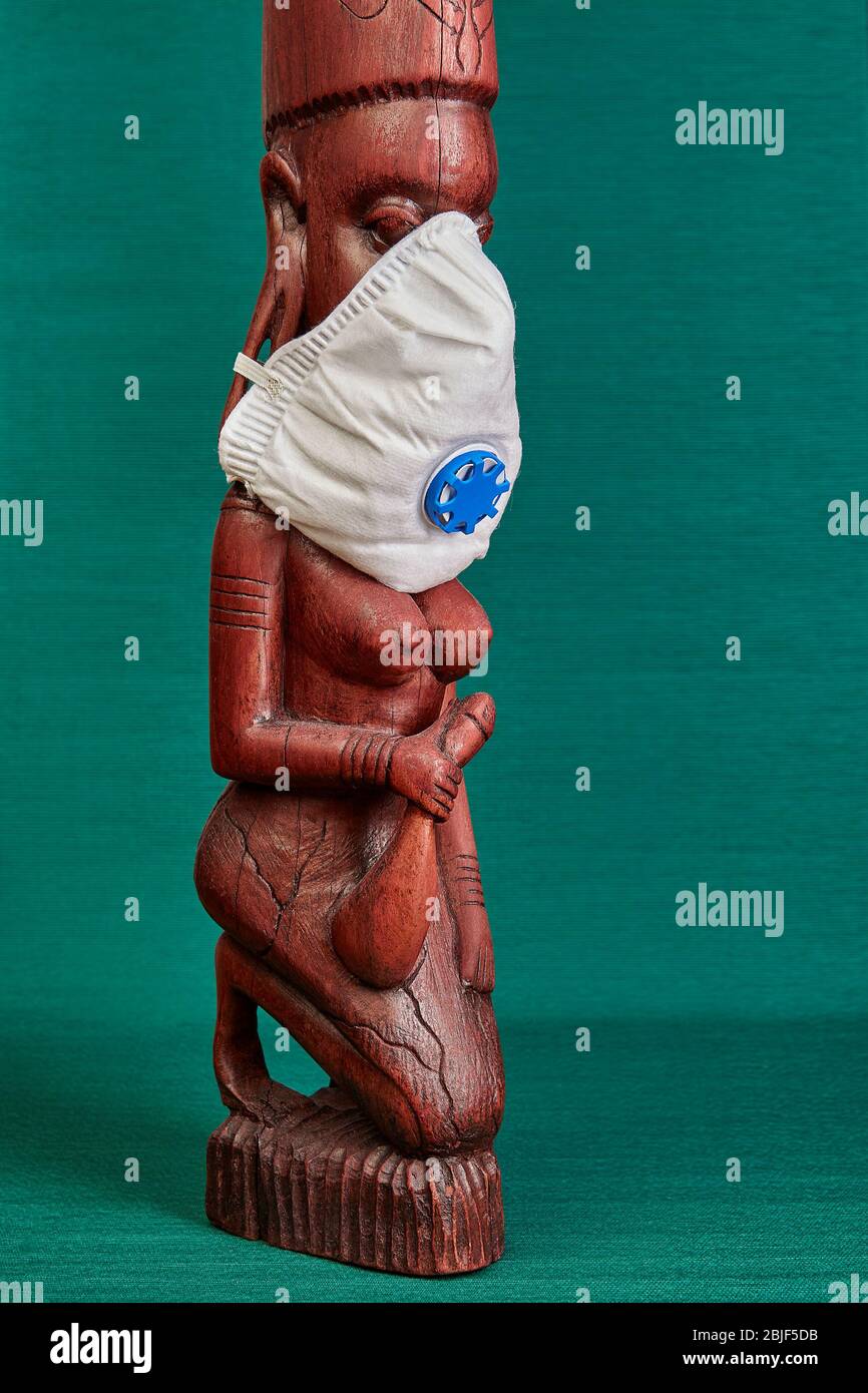 Carved wooden figurine as a souvenir for tourists traveling in Tanzania. A woman from Masai tribe wears an N95 respirator mask. Stock Photo