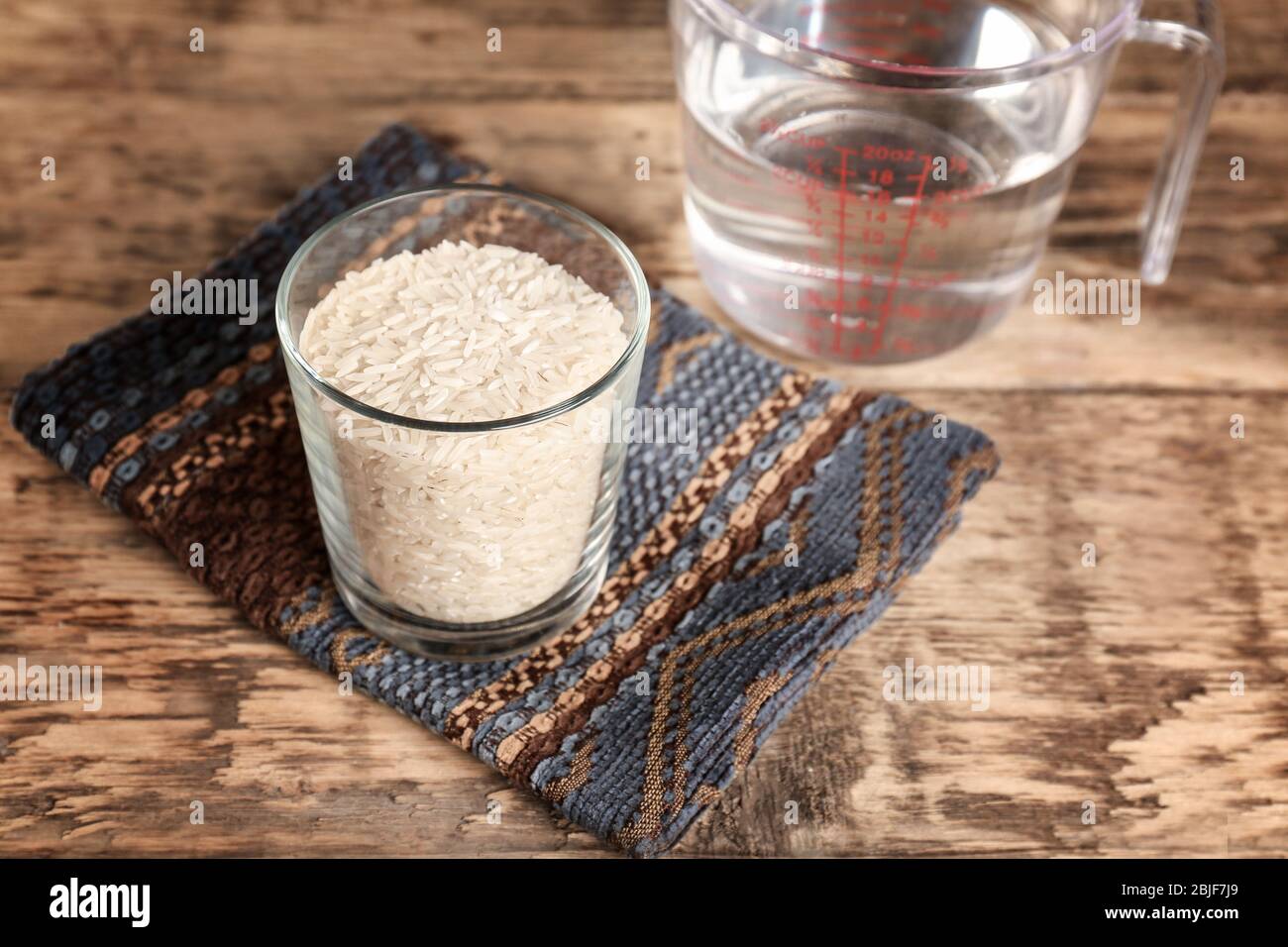 Glass of rice and measuring jug with water on wooden table Stock Photo