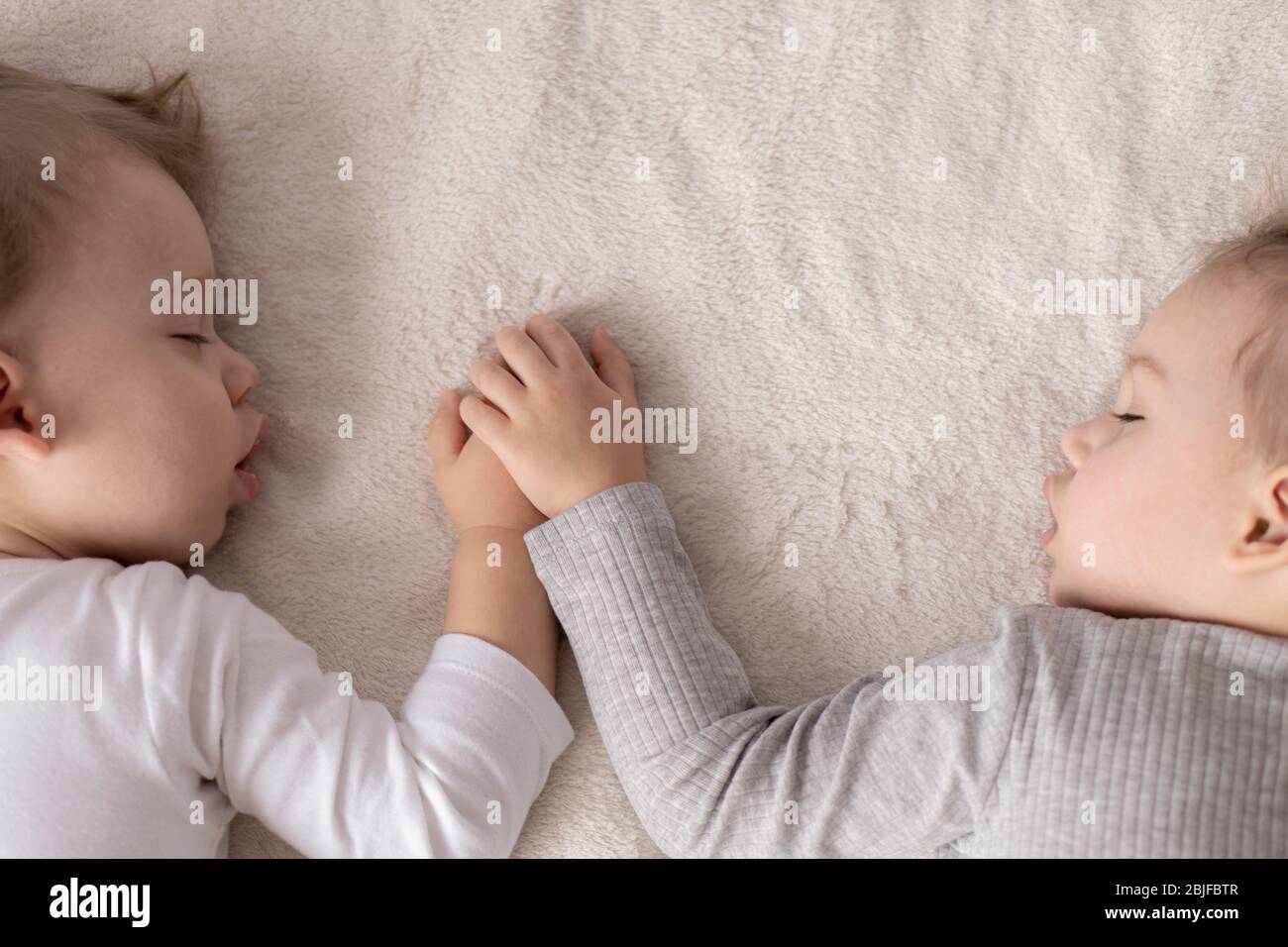 Childhood, sleep, relaxation, family, lifestyle concept - two young children 2 and 3 years old dressed in white and beige bodysuit sleep on a beige Stock Photo