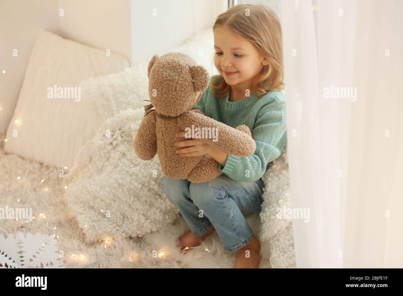 Cute little girl with teddy bear sitting on window sill at home Stock ...