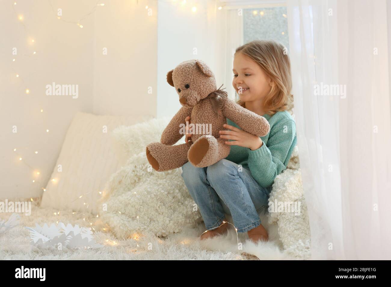 Cute little girl with teddy bear sitting on window sill at home Stock ...