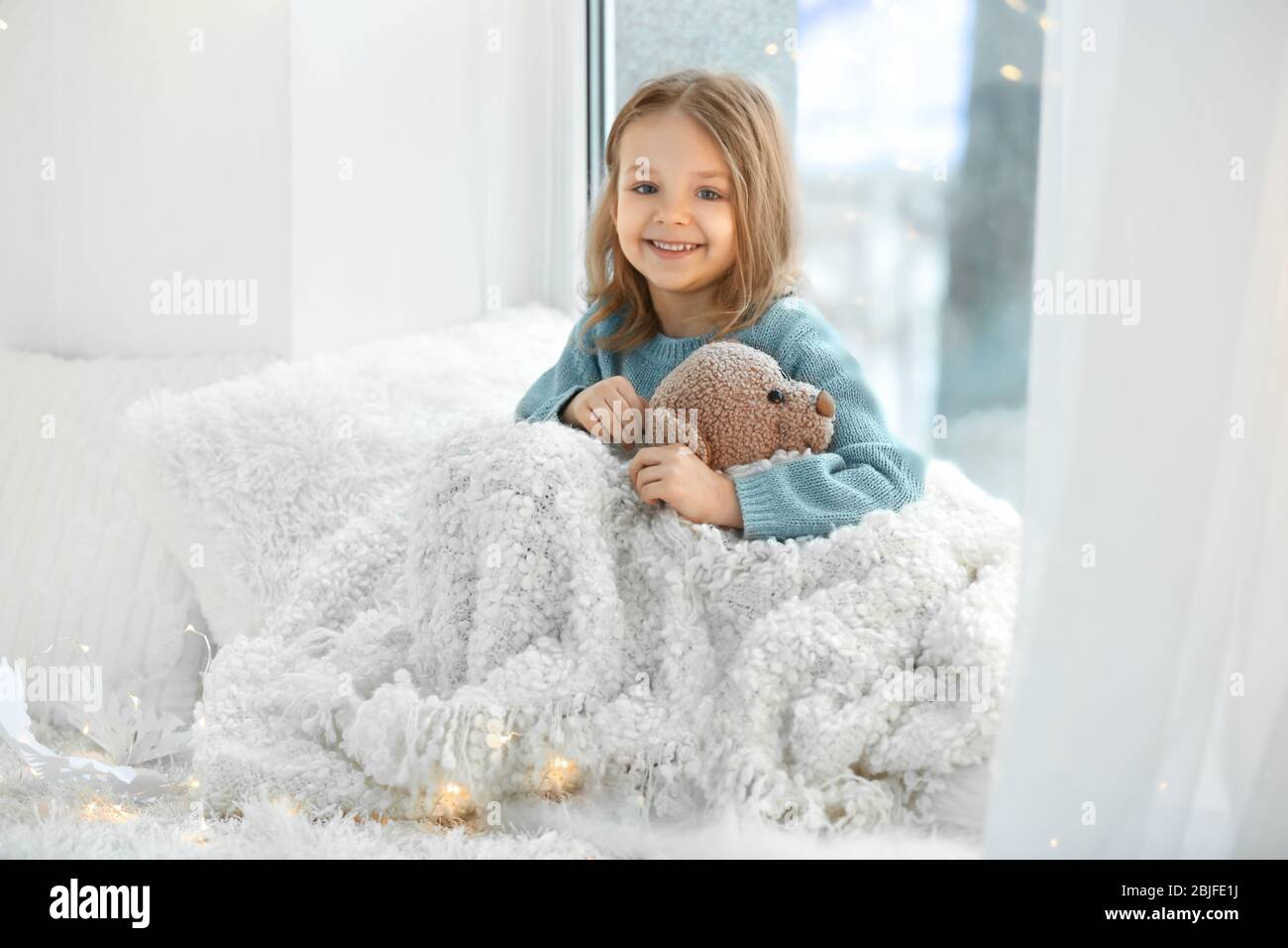 Cute little girl with teddy bear sitting on window sill at home Stock ...