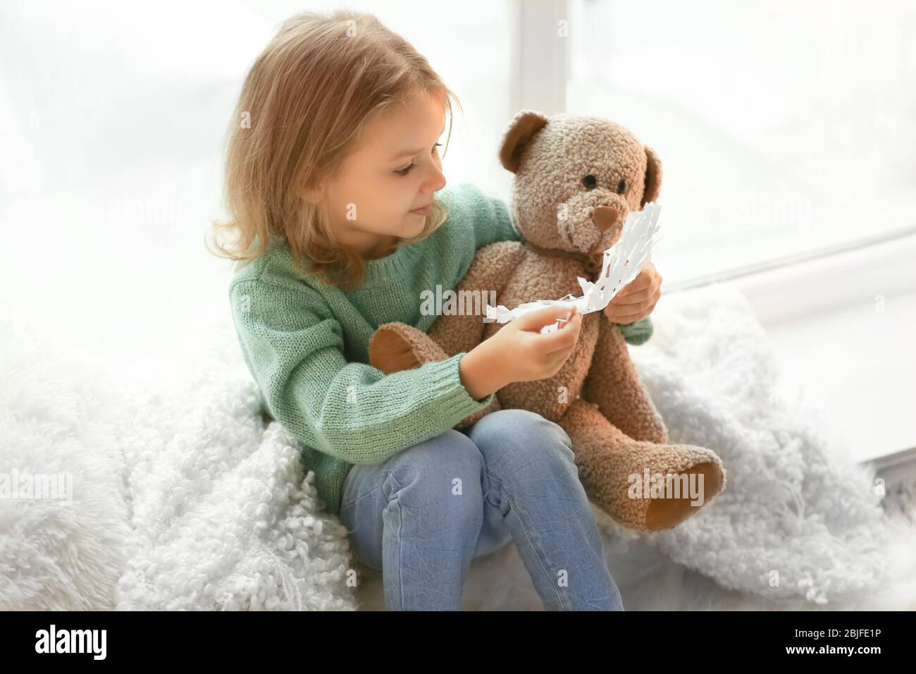Cute little girl with teddy bear sitting on window sill at home Stock ...