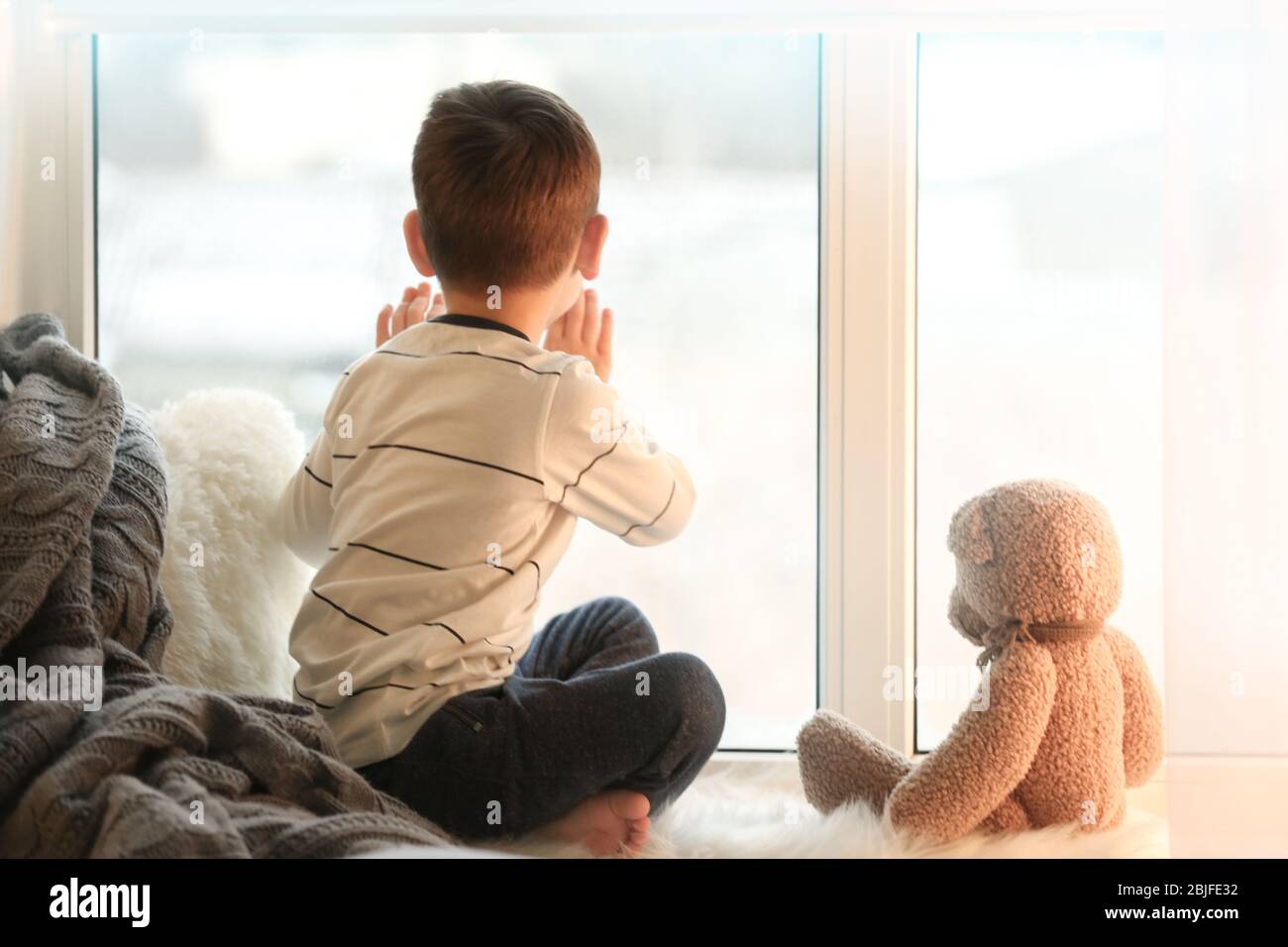 Cute little boy with teddy bear sitting on window sill at home Stock ...