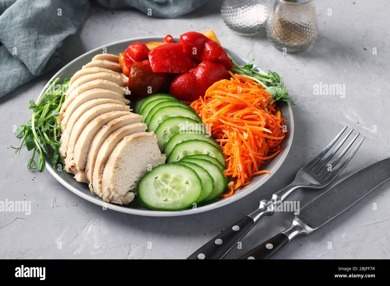 Buddha Bowl with baked chicken, fresh cucumber, peas microgrines, carrots and sweet pepper on a gray concrete background. Concept for clean and Stock Photo