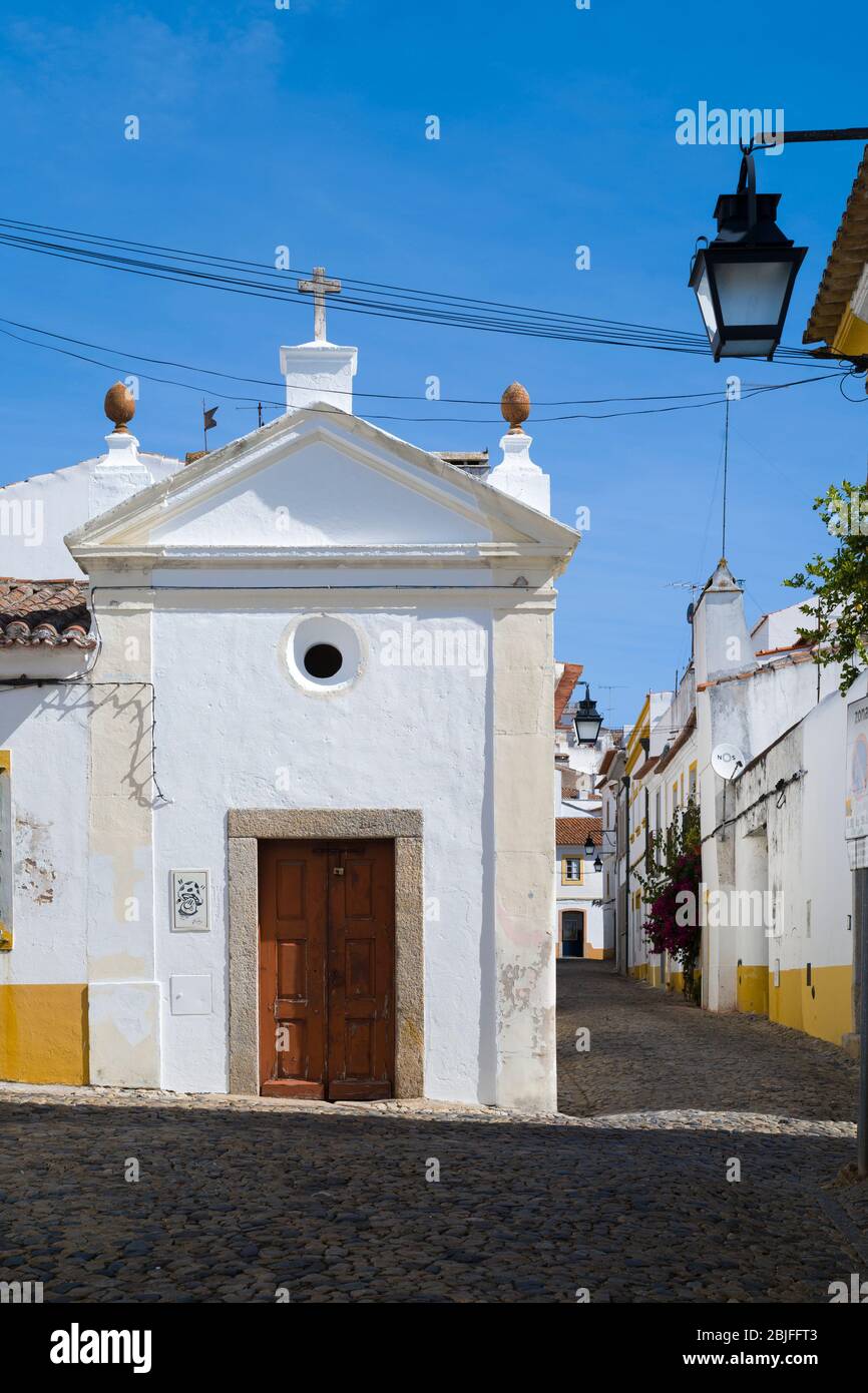 Typical street scene of white and yellow houses, lanterns and narrow cobble street in Evora, Portugal Stock Photo