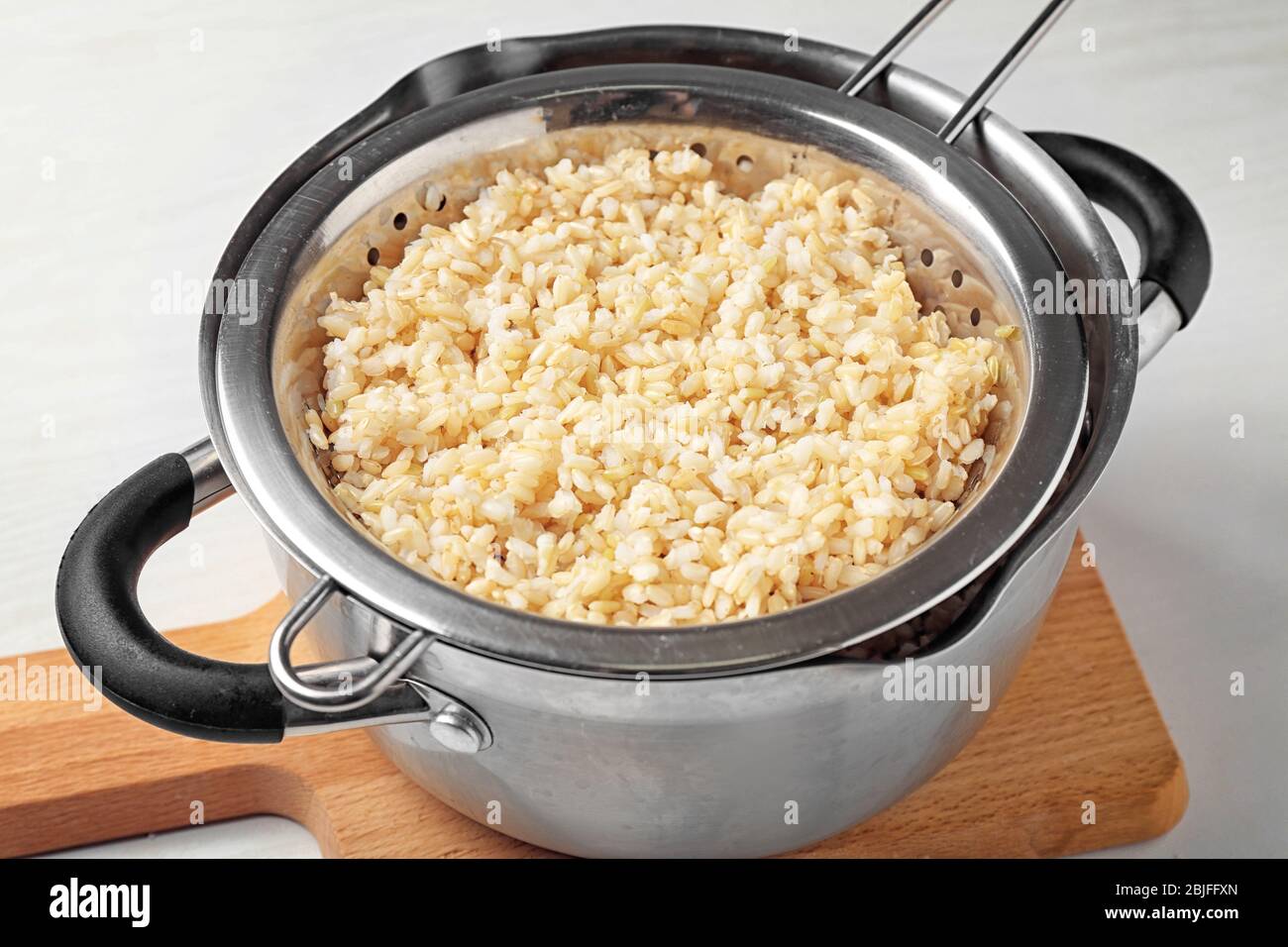 Colander with brown rice in saucepan on wooden board Stock Photo - Alamy