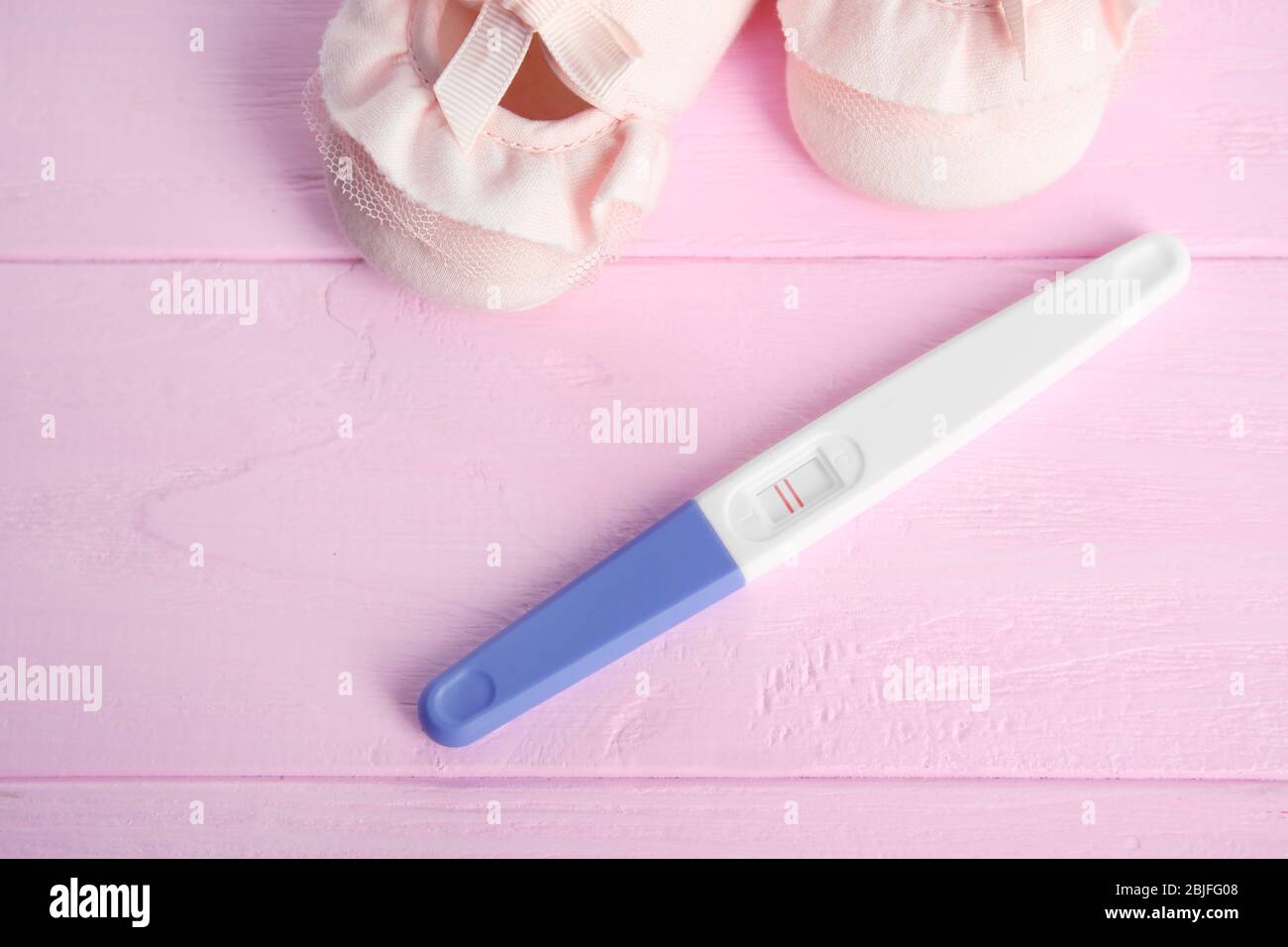 Pregnancy test and cute baby shoes on pink wooden background Stock