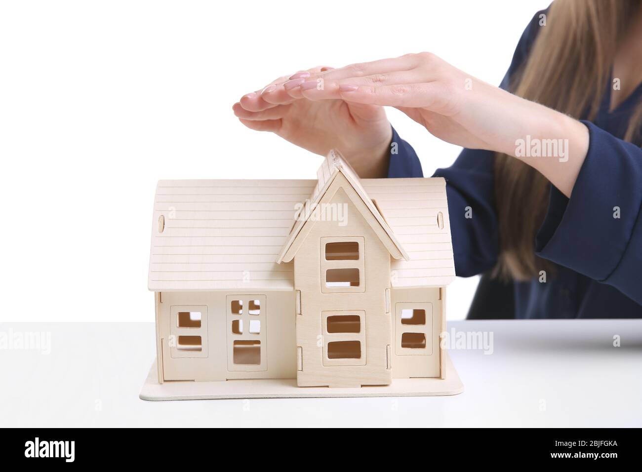 Woman holding hands under wooden model of house on table Stock Photo ...
