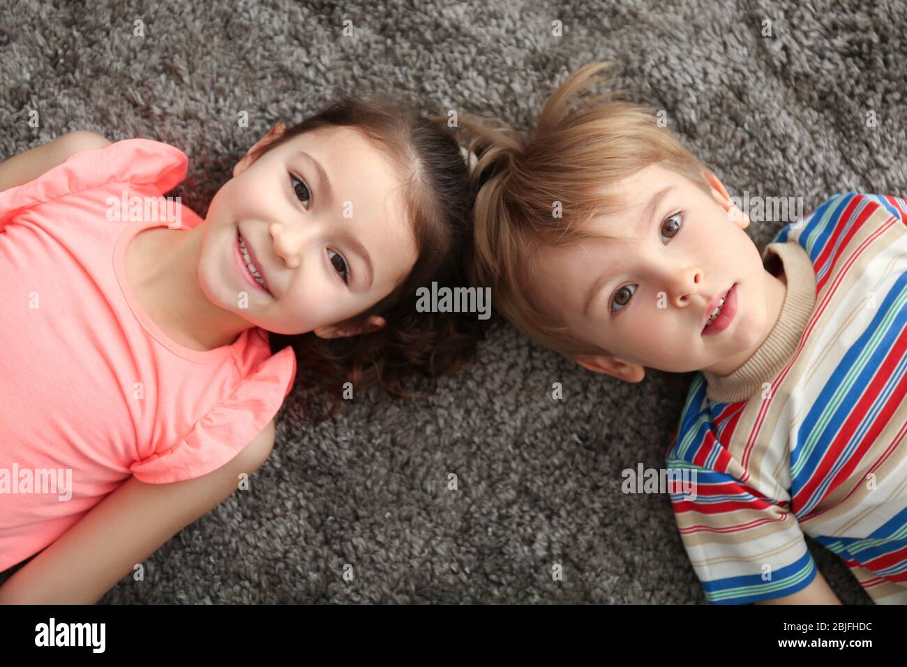 Cute little children lying on carpet at home Stock Photo - Alamy