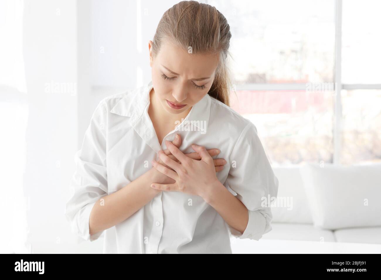 Heart attack concept. Young woman suffering from chest pain in office