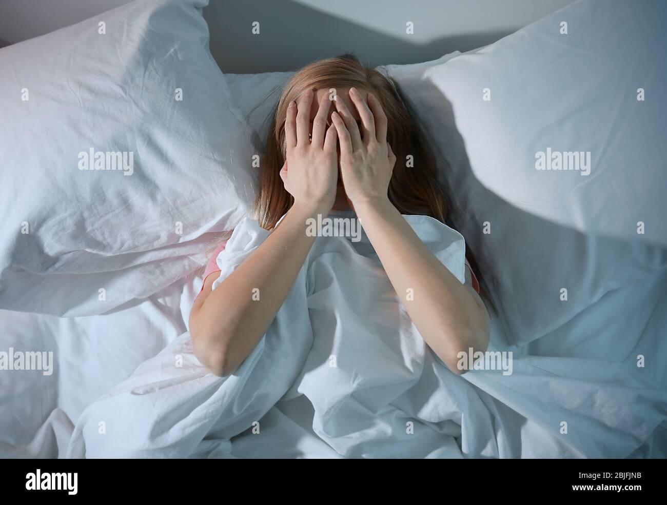 Young scared woman lying in bed at home Stock Photo