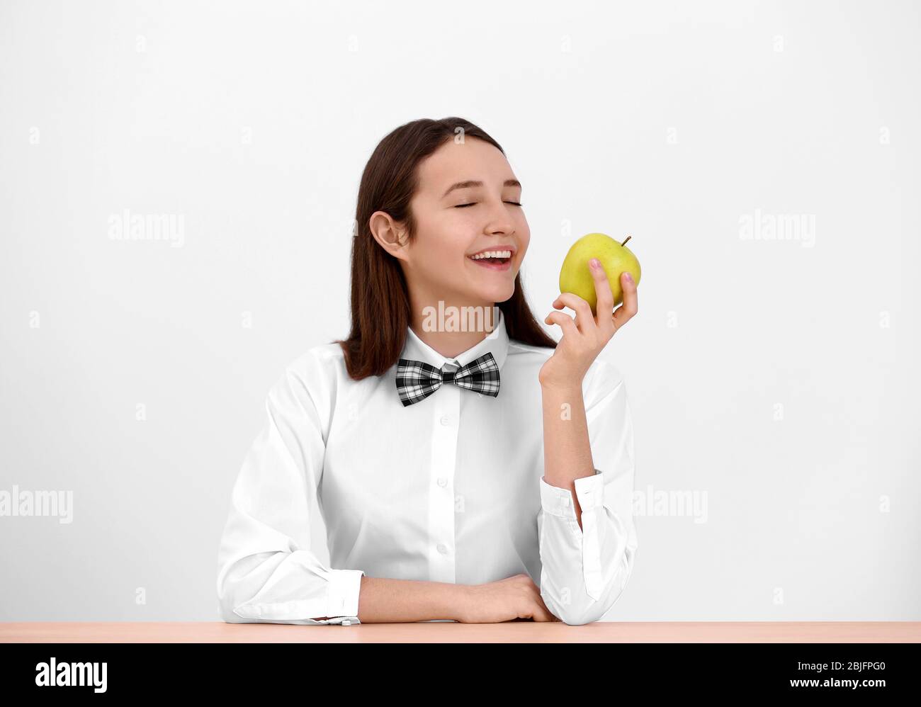 Cute schoolgirl with apple sitting at table in classroom Stock Photo ...