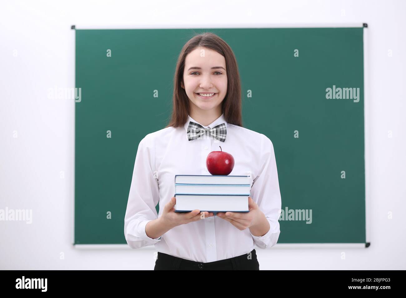 Cute schoolgirl with apple and books in classroom Stock Photo - Alamy