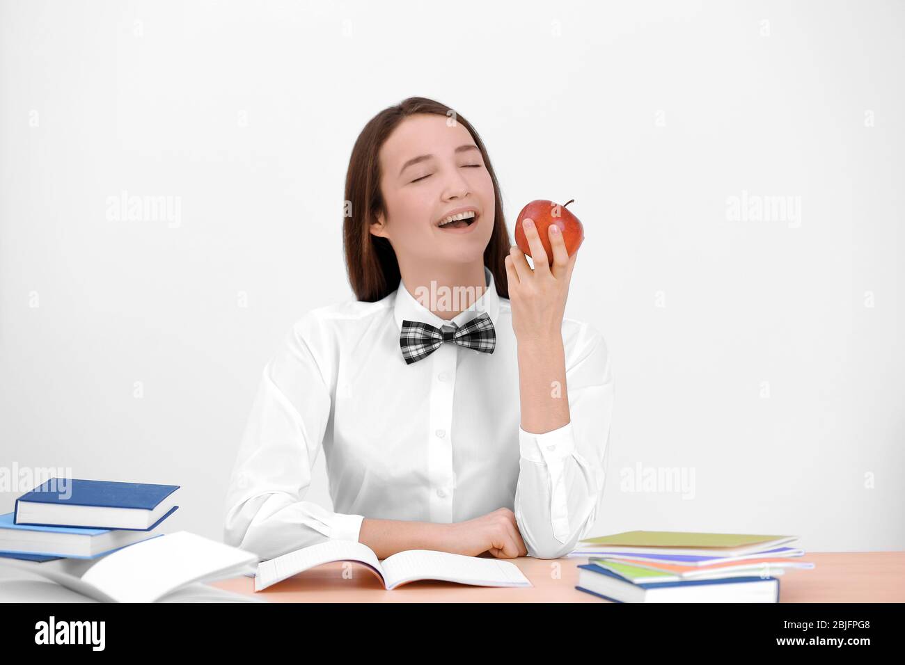 Cute schoolgirl with apple sitting at table in classroom Stock Photo ...