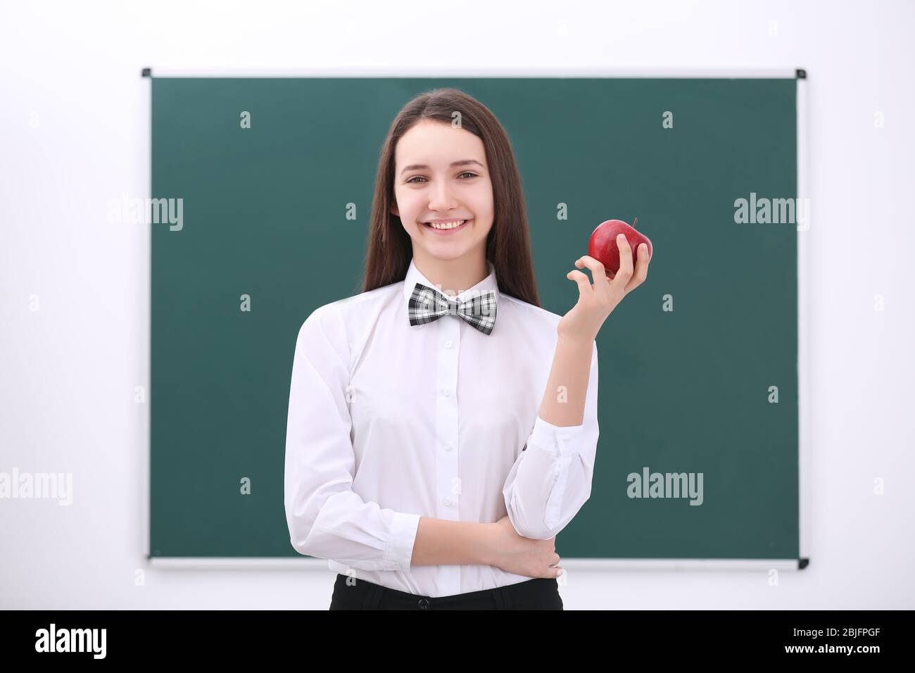 Cute schoolgirl with apple in classroom Stock Photo - Alamy
