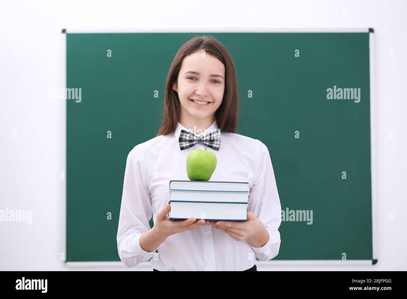 Cute schoolgirl with apple and books in classroom Stock Photo - Alamy