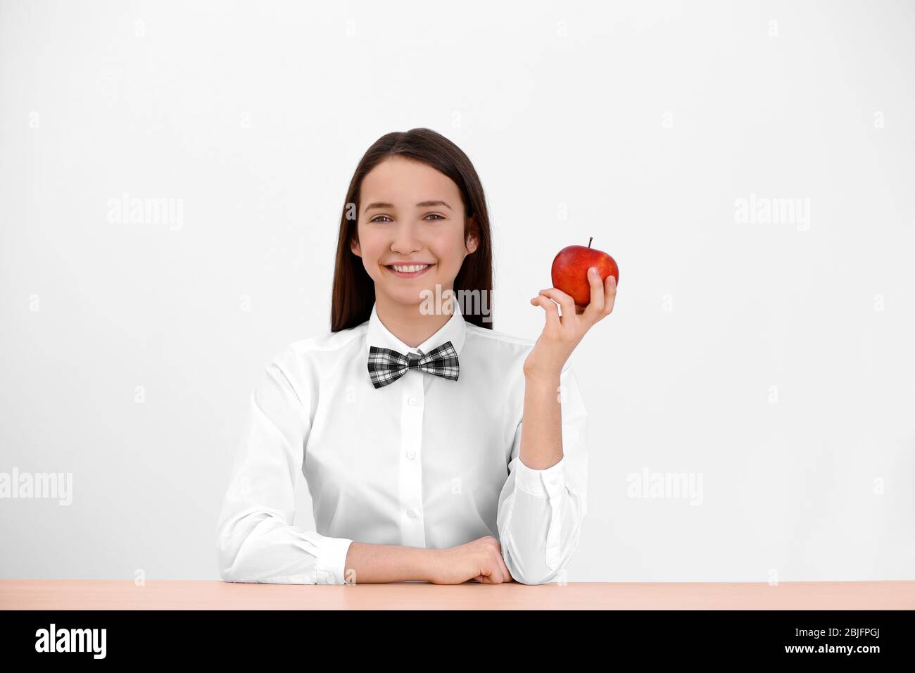 Cute schoolgirl with apple sitting at table in classroom Stock Photo ...