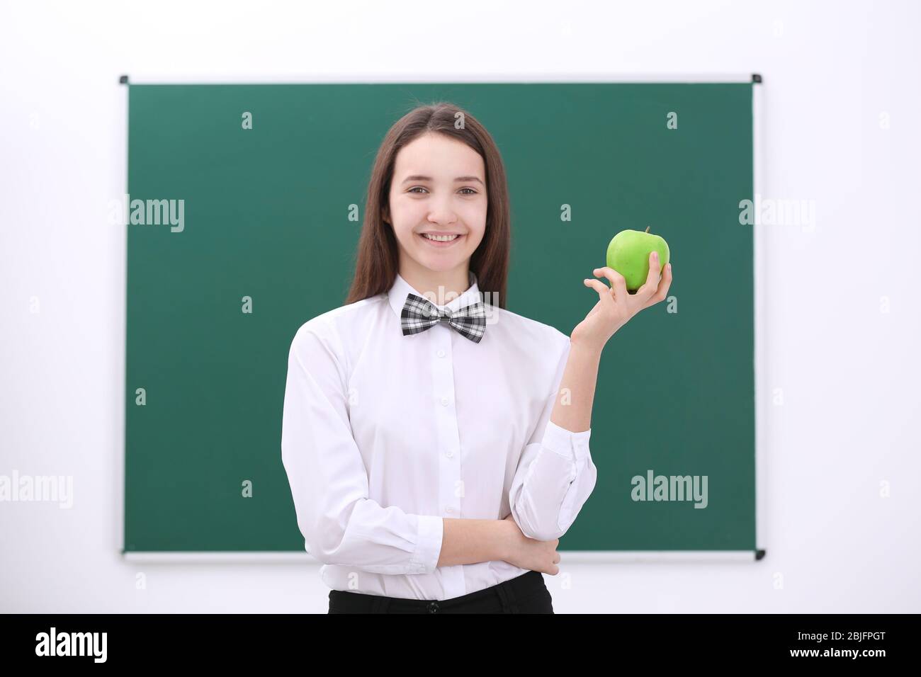 Cute schoolgirl with apple in classroom Stock Photo - Alamy