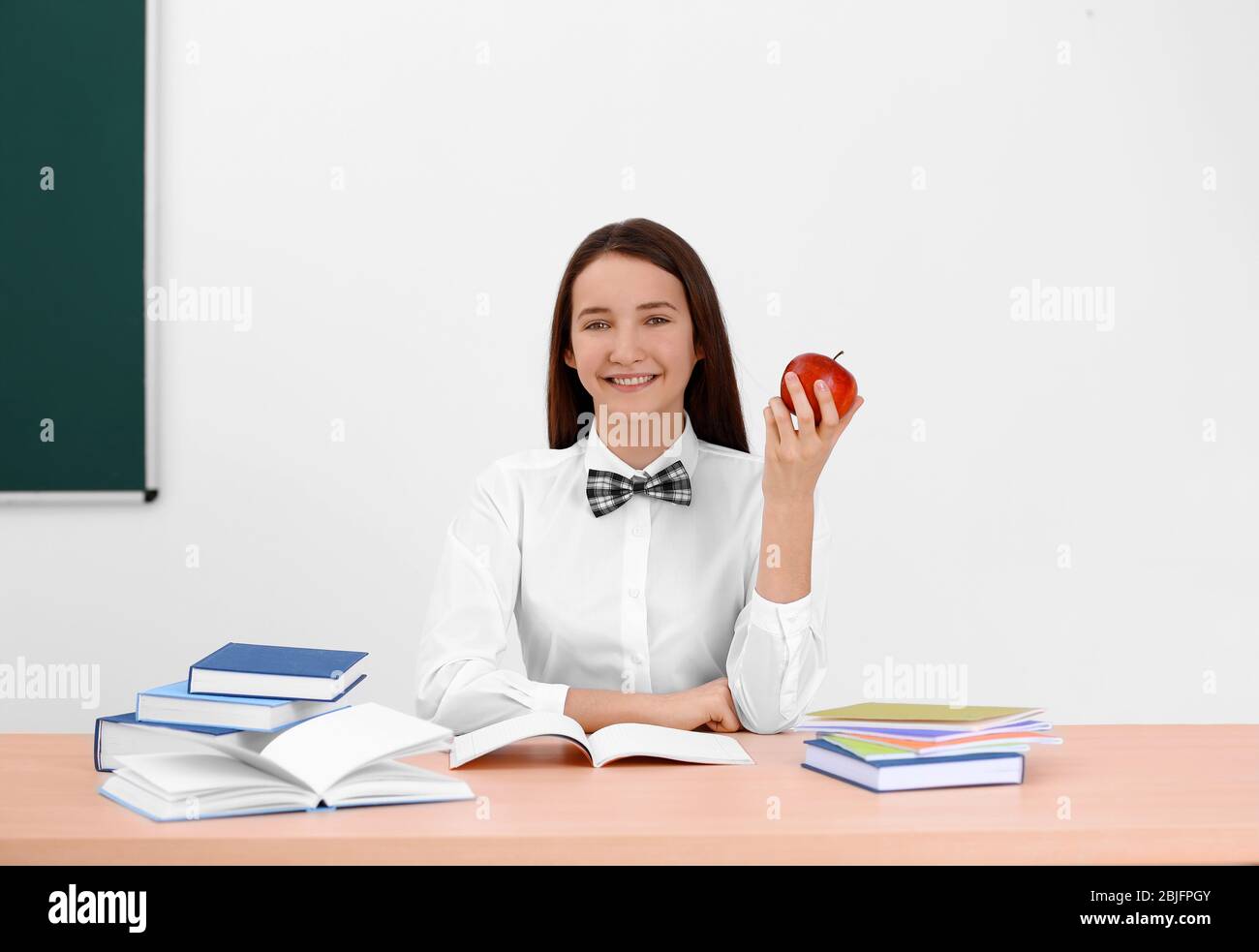 Cute schoolgirl with apple sitting at table in classroom Stock Photo ...