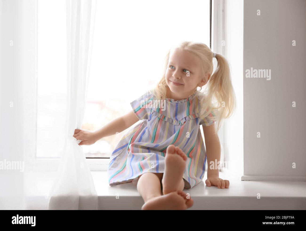 Cute little girl sitting on windowsill Stock Photo - Alamy
