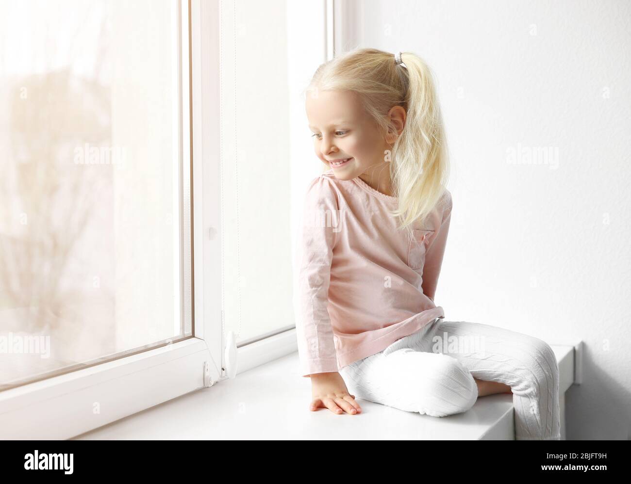 Cute little girl sitting on windowsill Stock Photo - Alamy
