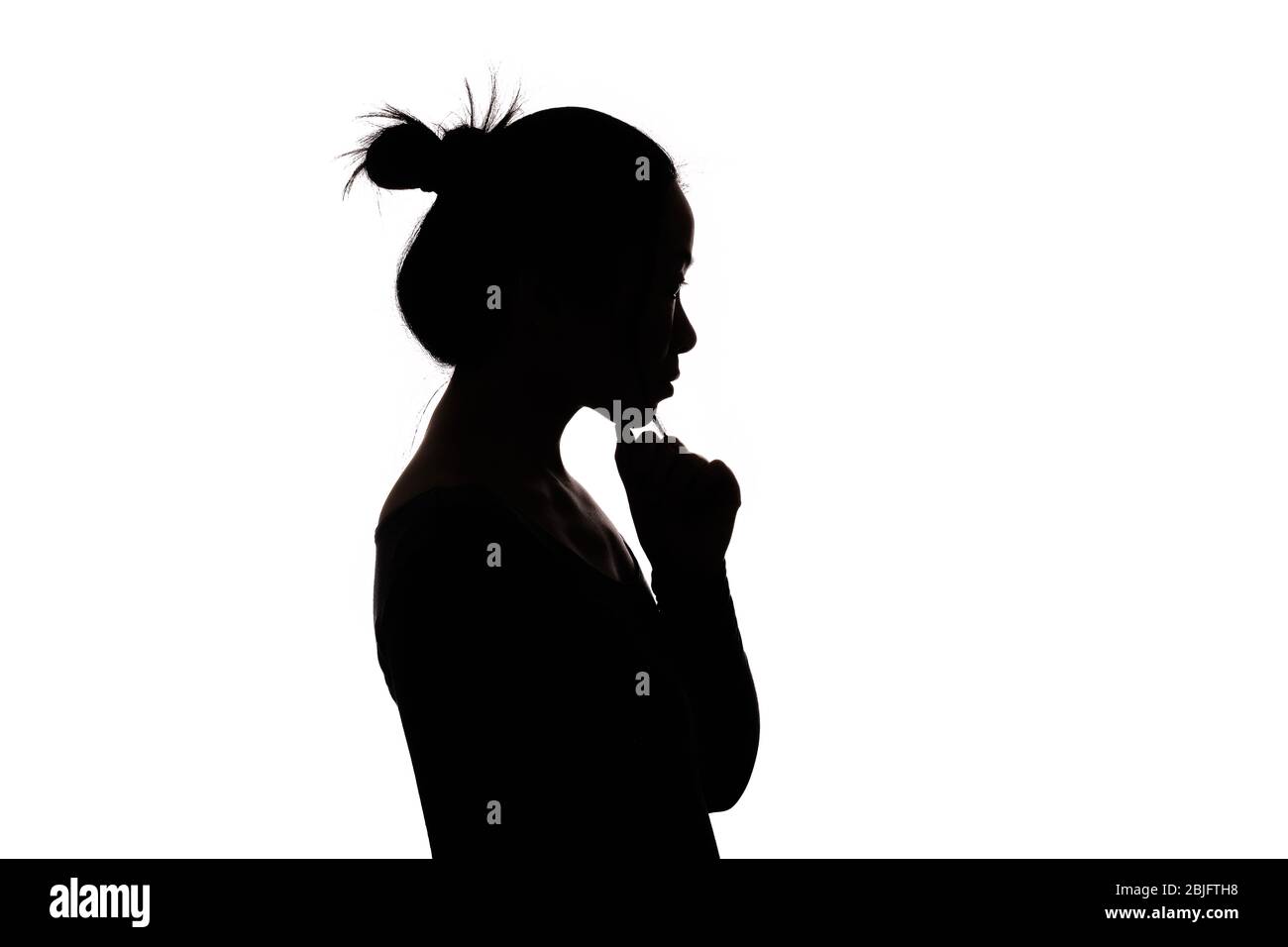 Black backlit silhouette of head and shoulders of an oriental woman from the side outlined by light Stock Photo