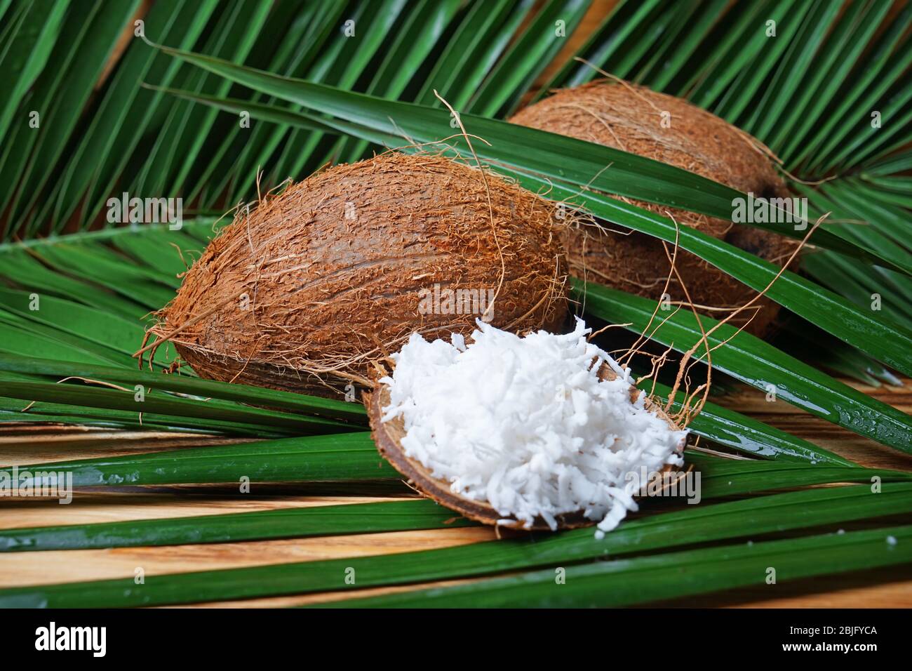 Fresh coconuts and flakes in rind on wooden background with palm leaves ...
