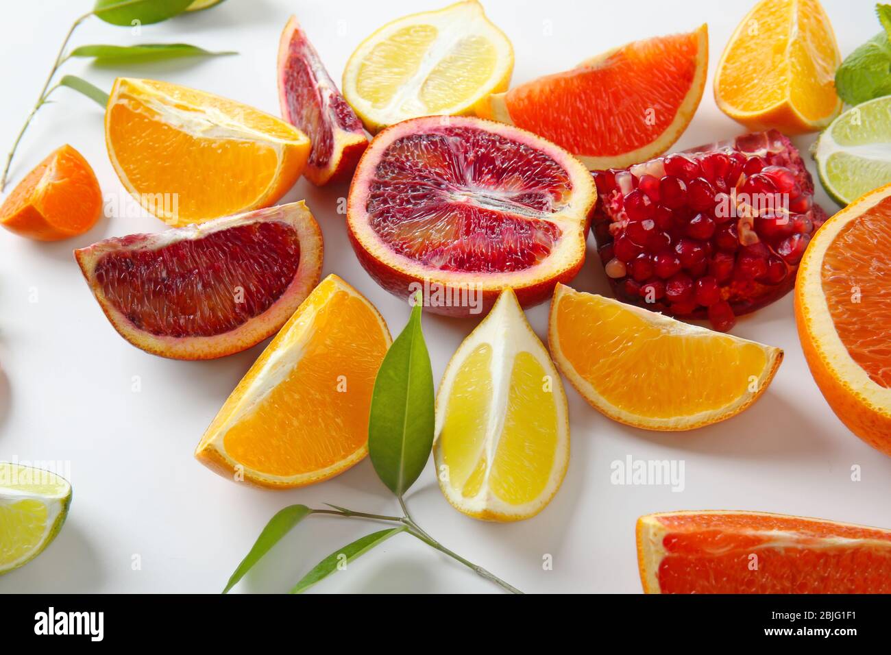 Composition of pomegranate and citrus fruits with green leaves on white ...