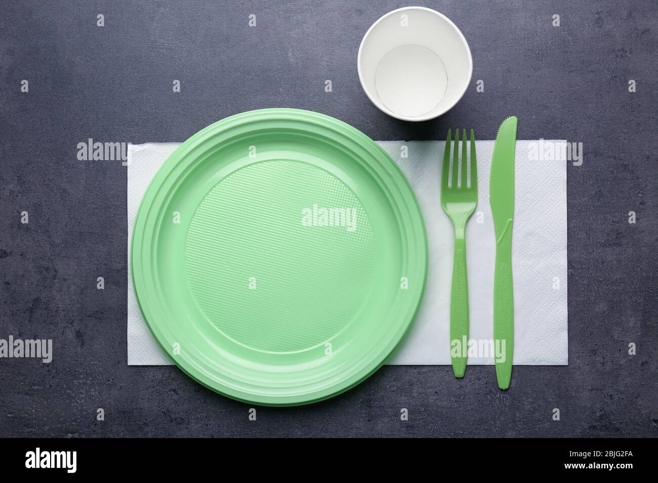 Green plastic disposable tableware on gray background Stock Photo