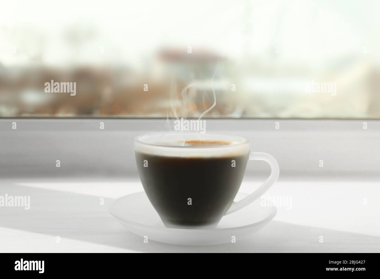 Matte glass cup of coffee on white window sill Stock Photo