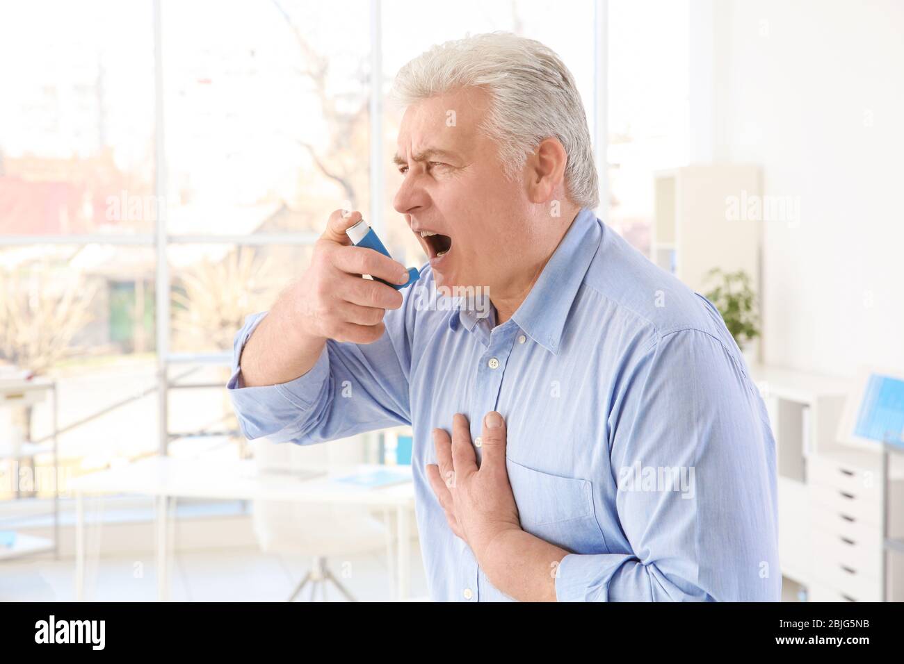 Elderly man using inhaler in clinic Stock Photo